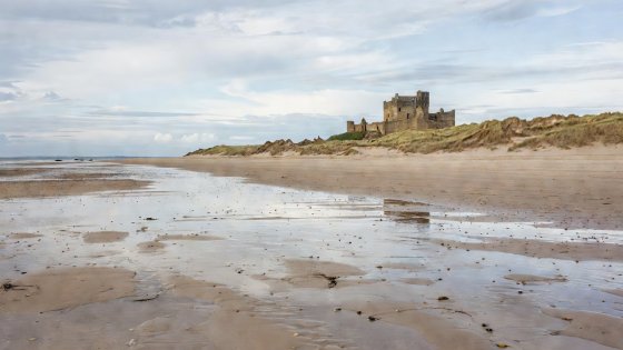 A wide sandy beach at low tide with a large sandstone castle perched on dunes in the distance